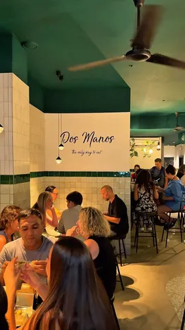 El local de DosManos lleno, con techo verde y azulejos blancos